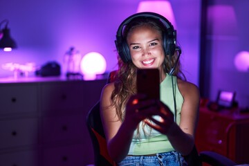 Young hispanic woman playing video games with smartphone looking positive and happy standing and smiling with a confident smile showing teeth