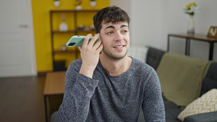 Young hispanic man listening to voice message smiling at home