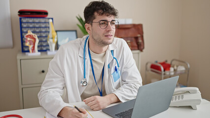 Young hispanic man doctor using laptop working at clinic