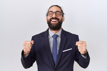 Hispanic man with beard wearing suit and tie excited for success with arms raised and eyes closed celebrating victory smiling. winner concept.