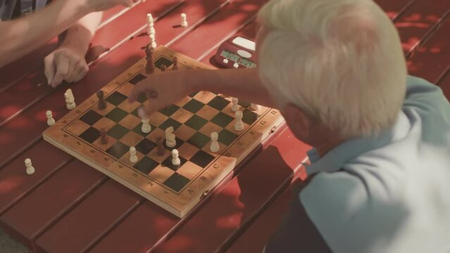 Two concentrated old men playing chess game outdoors, pressing button on chess clock after making moves