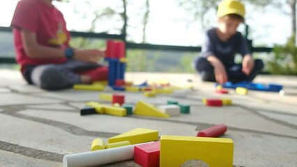 two sons play colorful wooden bricks sit on warm floor outdoor. Children development, babysitting job, leisure games on weekend at home concept
