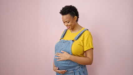 Young pregnant woman smiling confident touching belly over isolated pink background