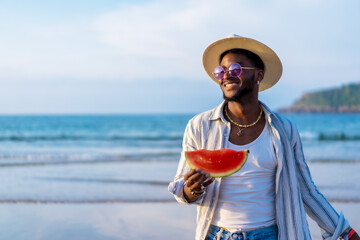 Portrait of a black ethnic man enjoy summer vacation at the beach eating a watermelon