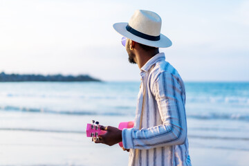 Black ethnic man enjoy summer vacation on the beach playing ukulele by the sea