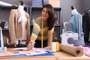 Middle age hispanic woman tailor drawing clothing design at atelier