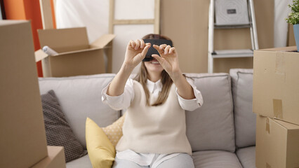 Young beautiful hispanic woman wearing virtual reality glasses sitting on the sofa at new home