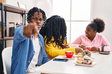 Group of three young black people sitting on a table having coffee pointing with finger to the camera and to you, confident gesture looking serious