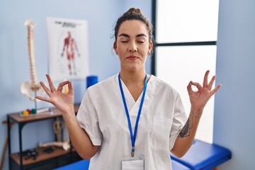 Young hispanic woman working at rehabilitation clinic relax and smiling with eyes closed doing meditation gesture with fingers. yoga concept.
