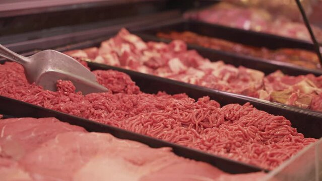 Tracking shot of red meat cuts and mincemeat in display fridge at a butchers shop.