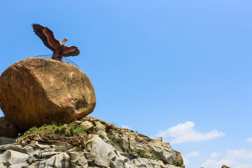 Eagle sitting on a rock on the background of blue sky. Rock craving. Jatayu Theme park Lepakshi