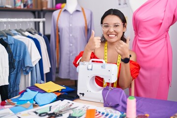 Hispanic young woman dressmaker designer using sewing machine success sign doing positive gesture...