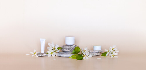 Natural anti-aging moisturizing spring cosmetics with flower extract and apple scent. Cream for eyelids, face and hands on stone pedestal or podium and fresh flowers of apple tree on pastel background