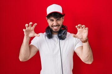 Hispanic man with beard wearing gamer hat and headphones smiling funny doing claw gesture as cat,...