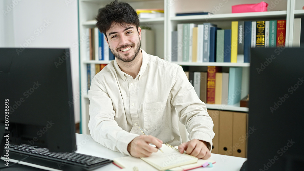 Wall mural Young hispanic man student using computer writing notes at library university