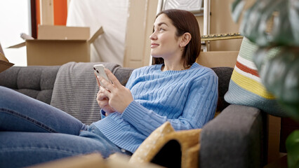 Fototapeta premium Young caucasian woman using smartphone sitting on sofa at new home