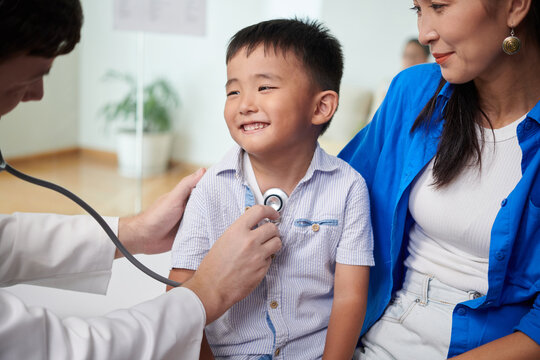 Smiling boy looking at doctor listening to his breath, visiting pediatrician concept