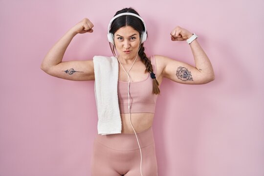 Young brunette woman wearing sportswear and headphones showing arms muscles smiling proud. fitness concept.