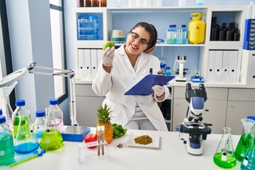 Young beautiful plus size woman scientist holding apple reading document at pharmacy