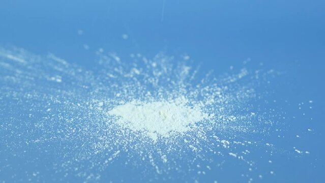 Silicon dioxide powder or Silica nanoparticles falling on blue surface, selective focus. Food additive E551, anti-caking agent. White chemical dust SiO2 used in food and cosmetics.