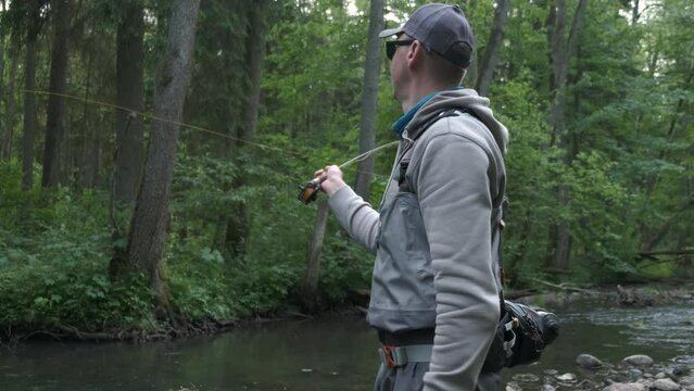 Fisherman catching brown trout on the fly standing in river. Slow motion. 