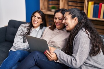 Three woman using laptop sitting on sofa at home