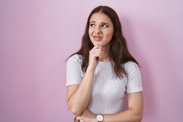 Young hispanic girl standing over pink background thinking worried about a question, concerned and nervous with hand on chin