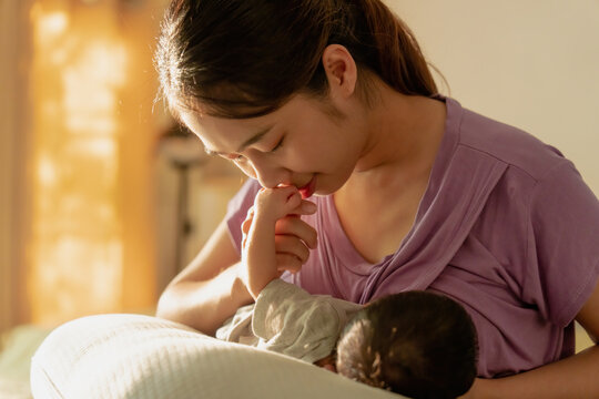 Asian mom is breastfeeding newborn at home.