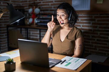 Young hispanic woman working at the office at night pointing finger up with successful idea. exited and happy. number one.