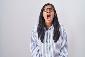 Young hispanic woman wearing glasses angry and mad screaming frustrated and furious, shouting with anger. rage and aggressive concept.