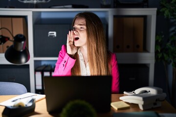 Young caucasian woman working at the office at night shouting and screaming loud to side with hand on mouth. communication concept.