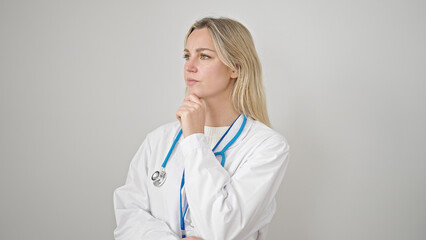 Young blonde woman doctor standing with doubt expression thinking over isolated white background