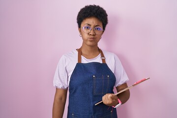 Young african american woman wearing professional waitress apron holding clipboard puffing cheeks with funny face. mouth inflated with air, crazy expression.