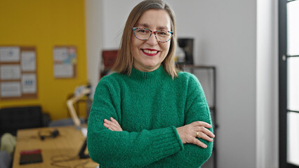 Mature hispanic woman with grey hair smiling confident with crossed arms at office