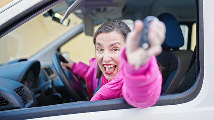 Fototapeta premium Mature hispanic woman with grey hair smiling confident holding key of new car at street