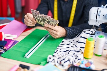 Young caucasian man tailor holding dollars at clothing factory