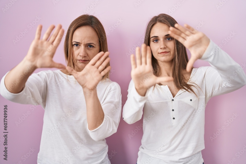 Canvas Prints Middle age mother and young daughter standing over pink background doing frame using hands palms and fingers, camera perspective