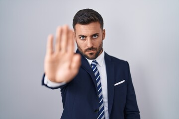 Handsome hispanic man wearing suit and tie doing stop sing with palm of the hand. warning expression with negative and serious gesture on the face.
