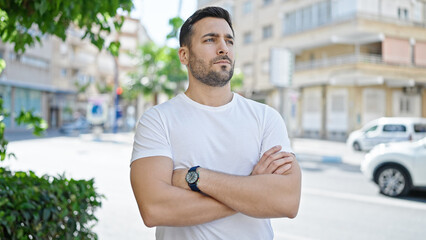 Fototapeta premium Young hispanic man standing with crossed arms and relaxed expression at street