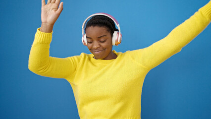 Naklejka premium African american woman dancing wearing headphones over isolated blue background