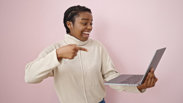 African american woman smiling pointing to laptop over isolated pink background