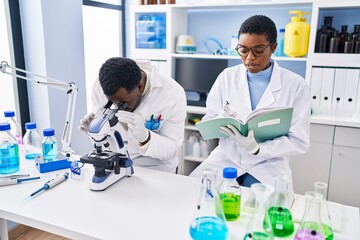 Man and woman scientists using microscope writing on notebook at laboratory