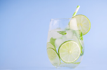 Summer lemonade with basil and lime on light blue background. One fresh summer cocktail with basil, green lemon and ice cubes. Drink concept