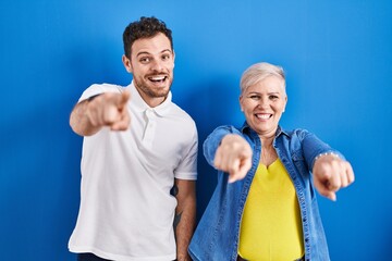 Young brazilian mother and son standing over blue background pointing to you and the camera with fingers, smiling positive and cheerful