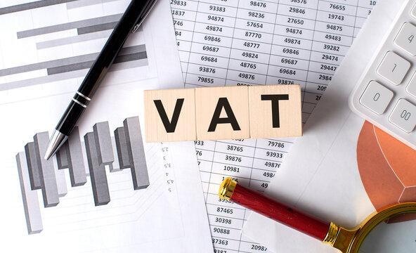 VAT text on wooden block on graph background with pen and magnifier
