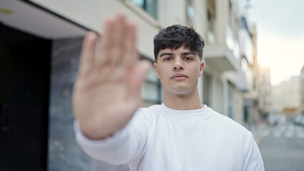 Young hispanic man doing stop gesture with hand at street