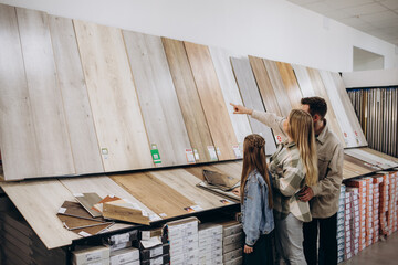 Modern family couple standing together with sample of laminated flooring in building store