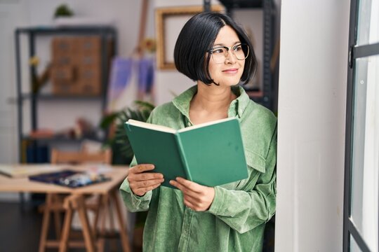 Young chinese woman artist smiling confident reading book at art studio