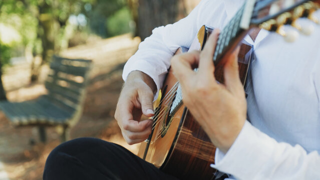 Professional guitarist plays guitar outdoors. Musician plays a classical guitar in the park. A man in a white shirt plays a musical instrument outside the house. The guitarist plays the guitar.