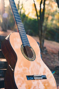 Beautiful classical guitar on a bench in the park with lens flare. Photo of a new wooden guitar with nylon strings outdoors in the summer during sunset. No people. Beautiful string instrument.